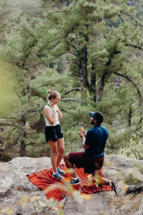 Man proposes to woman on blanket after hiking.