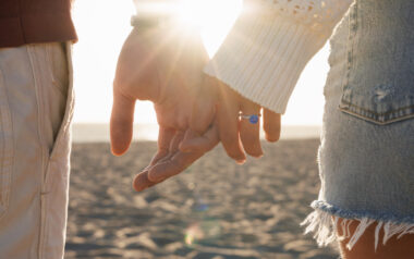 couple holding hands on the beach, the sun shining through their arms