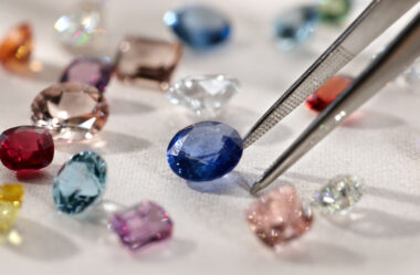 tweezers selecting a blue sapphire from a table with many different colored sapphires surrounding it